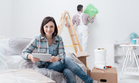 a-contractor-painting-wall-green-behind-a-women-sitting-on-a-couch-wondering-where-to-start-her-home-renovation-in-edmonton