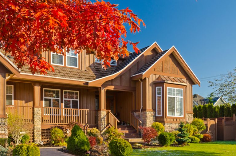 wood sided brick accented house with red maple tree in yard. green bushes and lawn. blue sky and golden light.