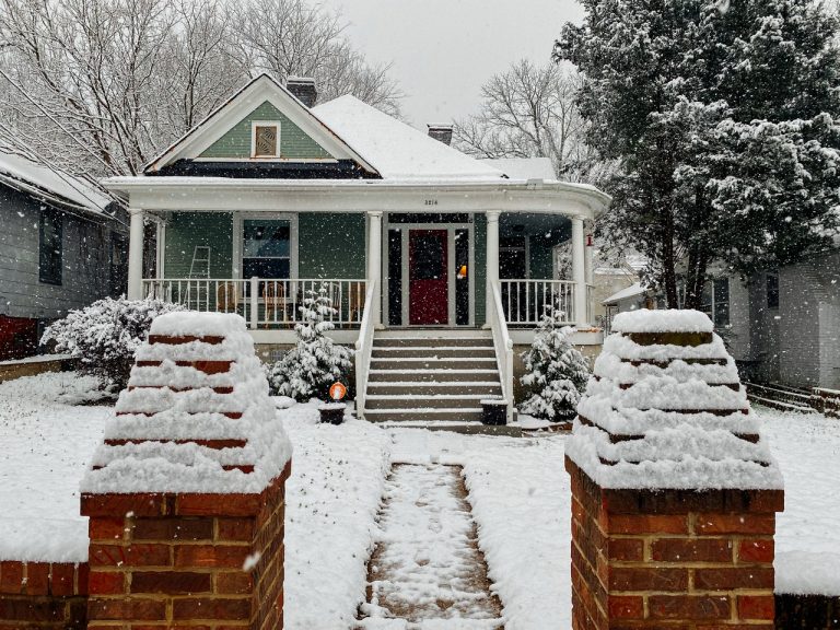 house with white trim and white stairs on a snowy day. red brick fence.