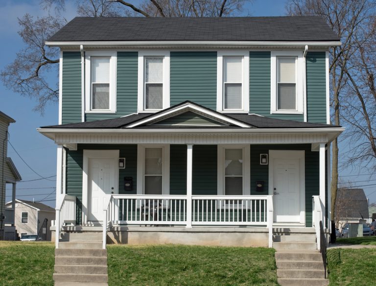 maritime style duplex with dark green siding, white trim. twin staircases lead down.