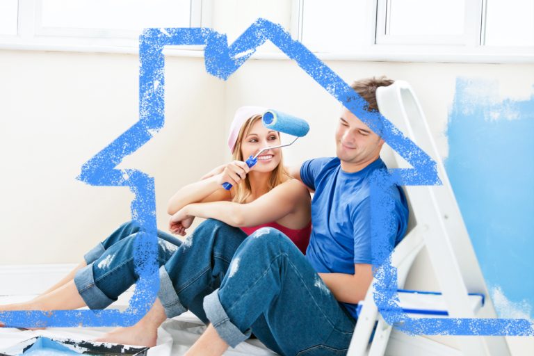 young couple sitting in white room holding blue paint rollers